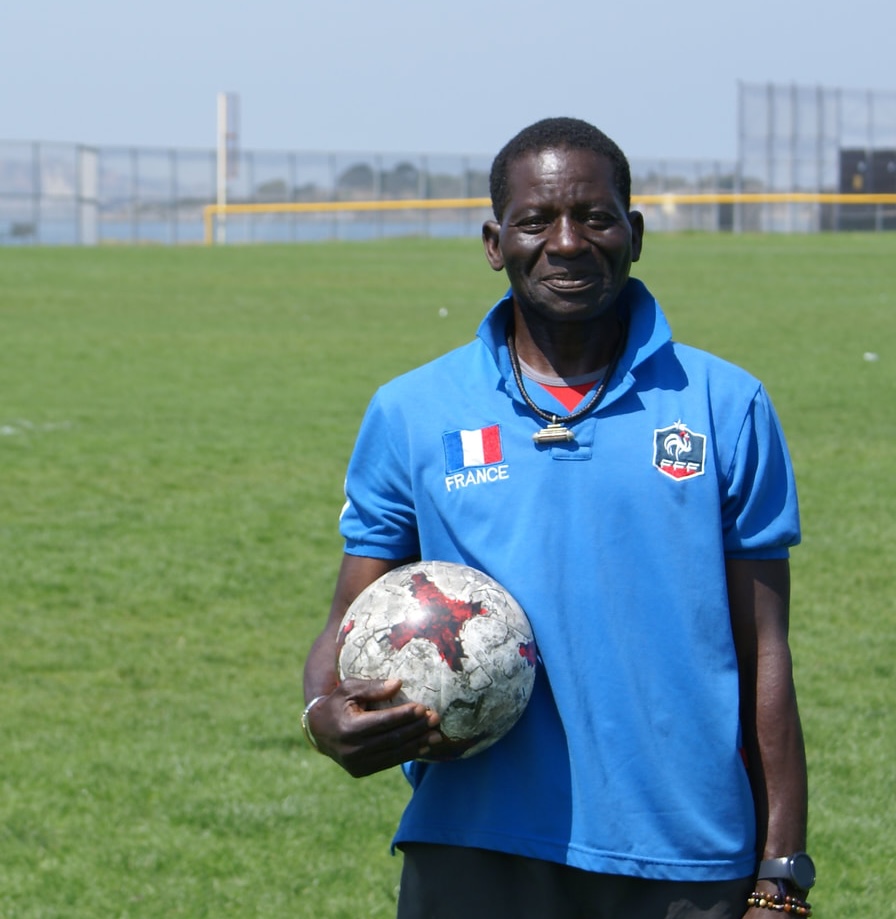 Djibril holding a soccer ball, on a field in front of the San Francisco Bay