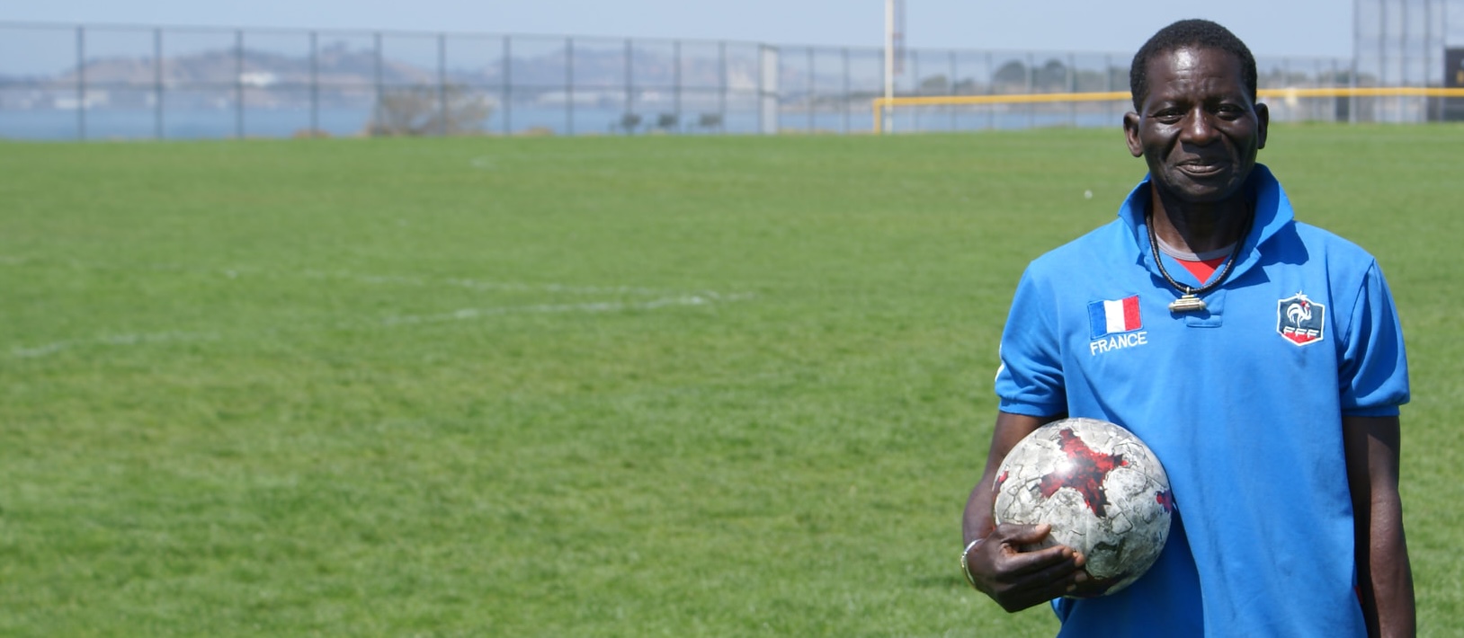 Djibril holding a soccer ball, on a field in front of the San Francisco Bay